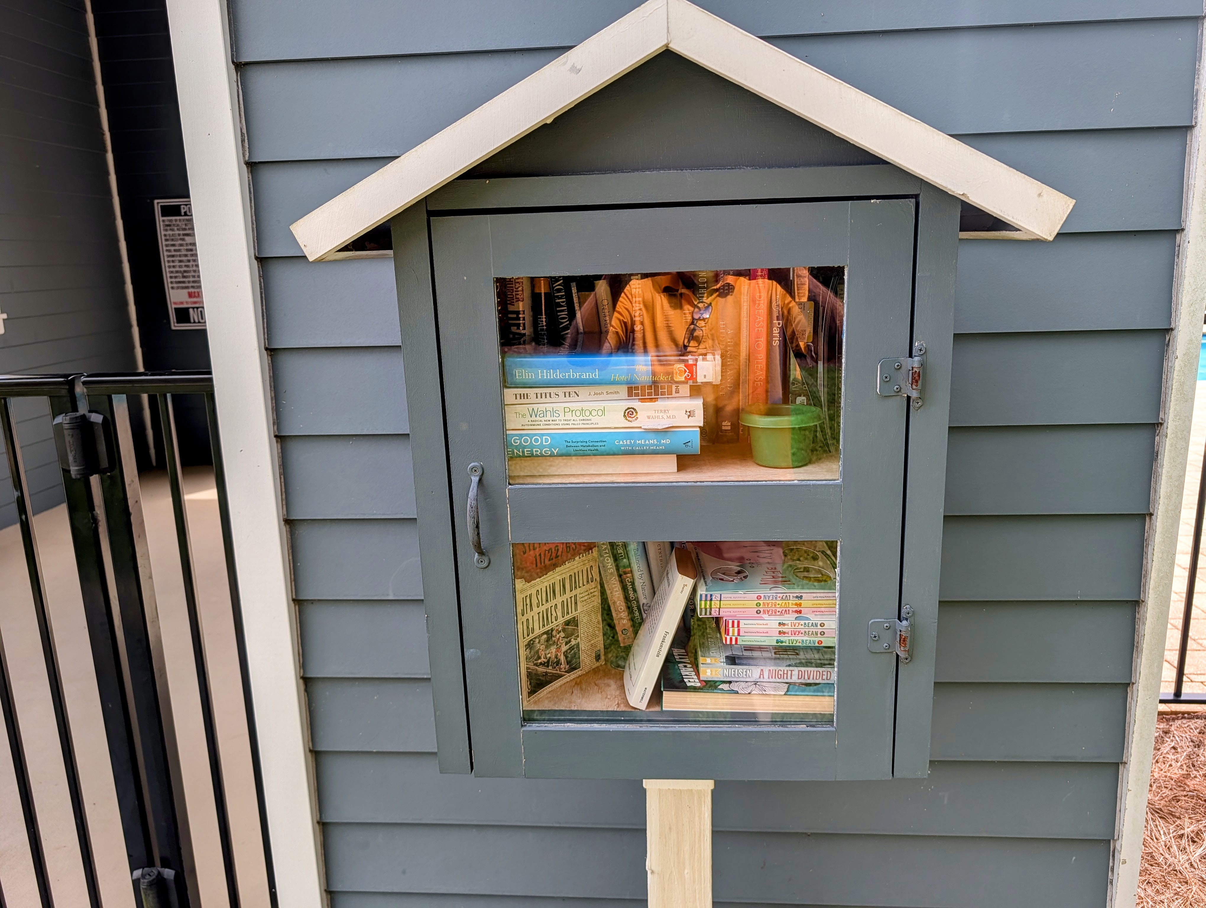 A small gabled share-a-book box mounted on a post beside the Paradise Cove pool deck, stocked with paperbacks